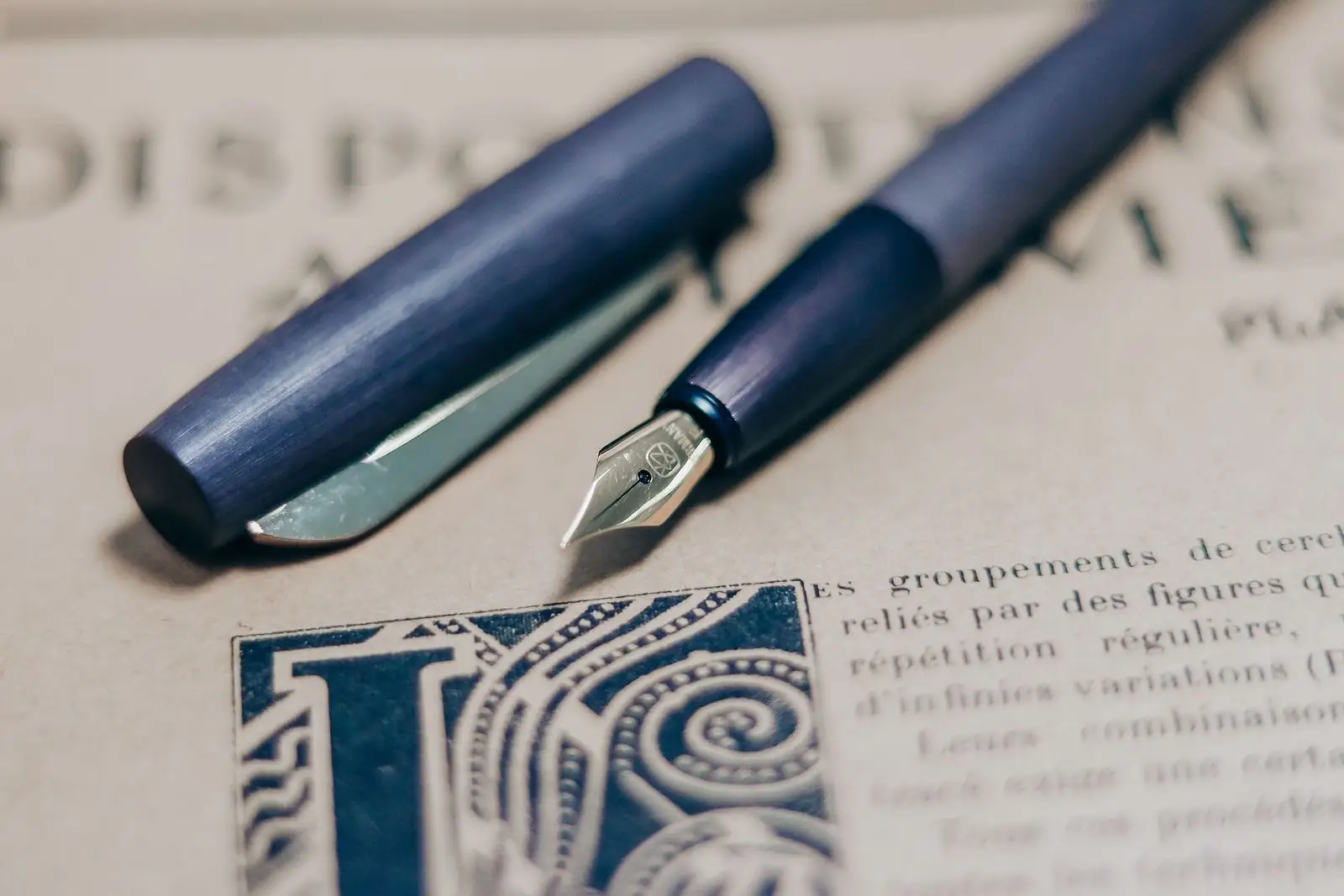 Blue fountain pen and cap resting on a printed page with an ornate initial letter