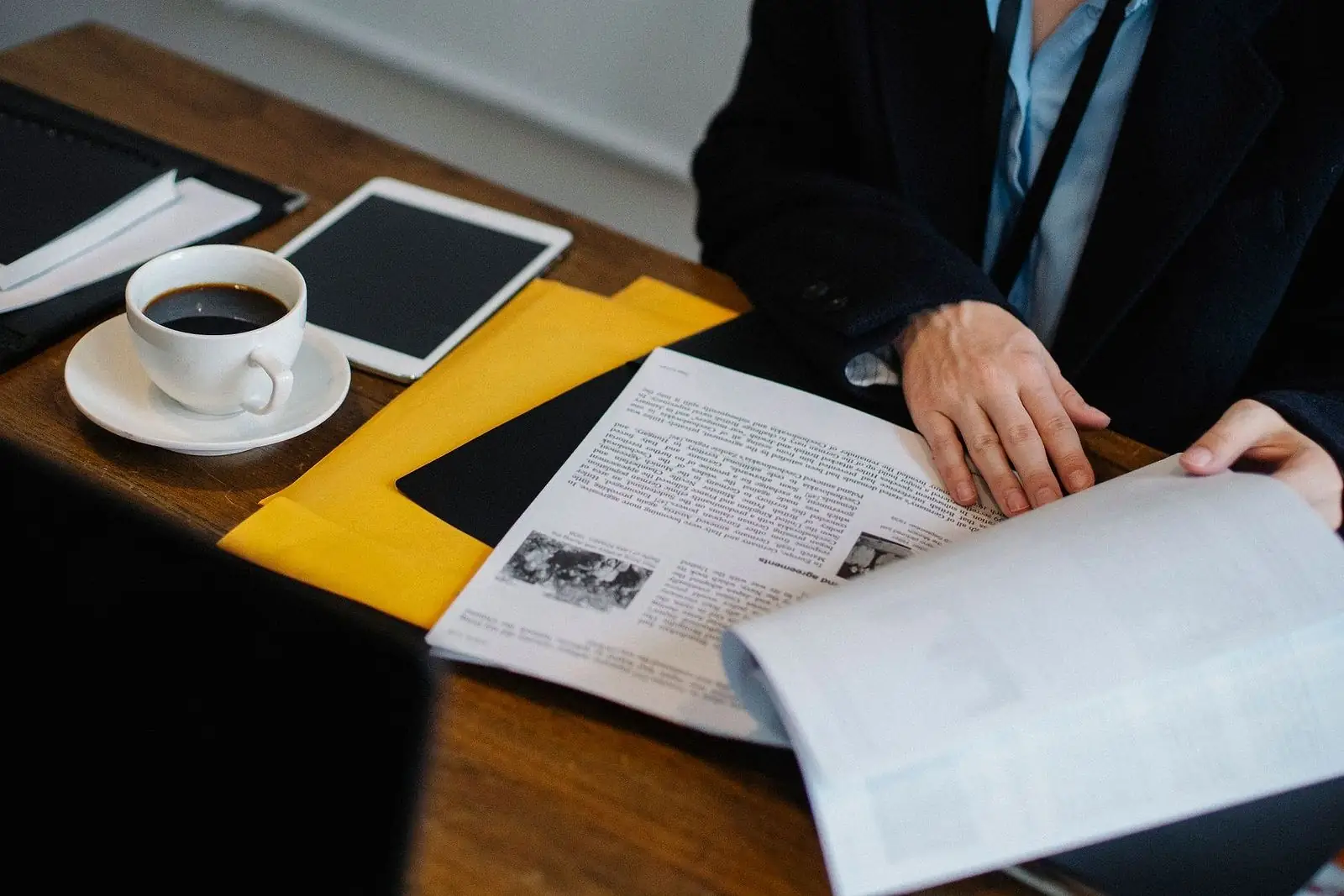 Hands turning the pages of a printed document at a desk with a tablet and coffee