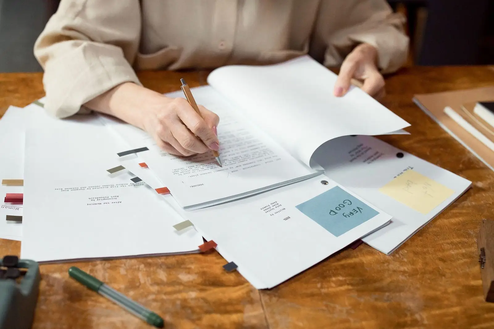 Hands marking up a printed manuscript with a pencil on a wooden desk, sticky notes and tabs