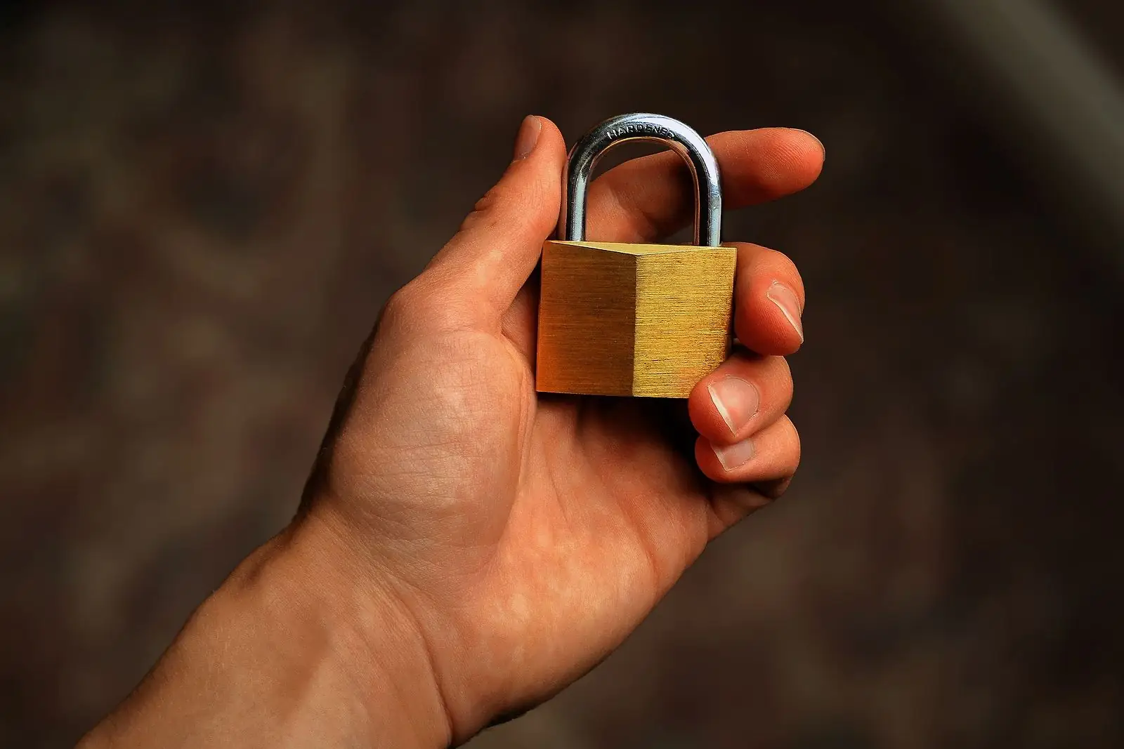 Hand holding a small brass padlock against a dark background