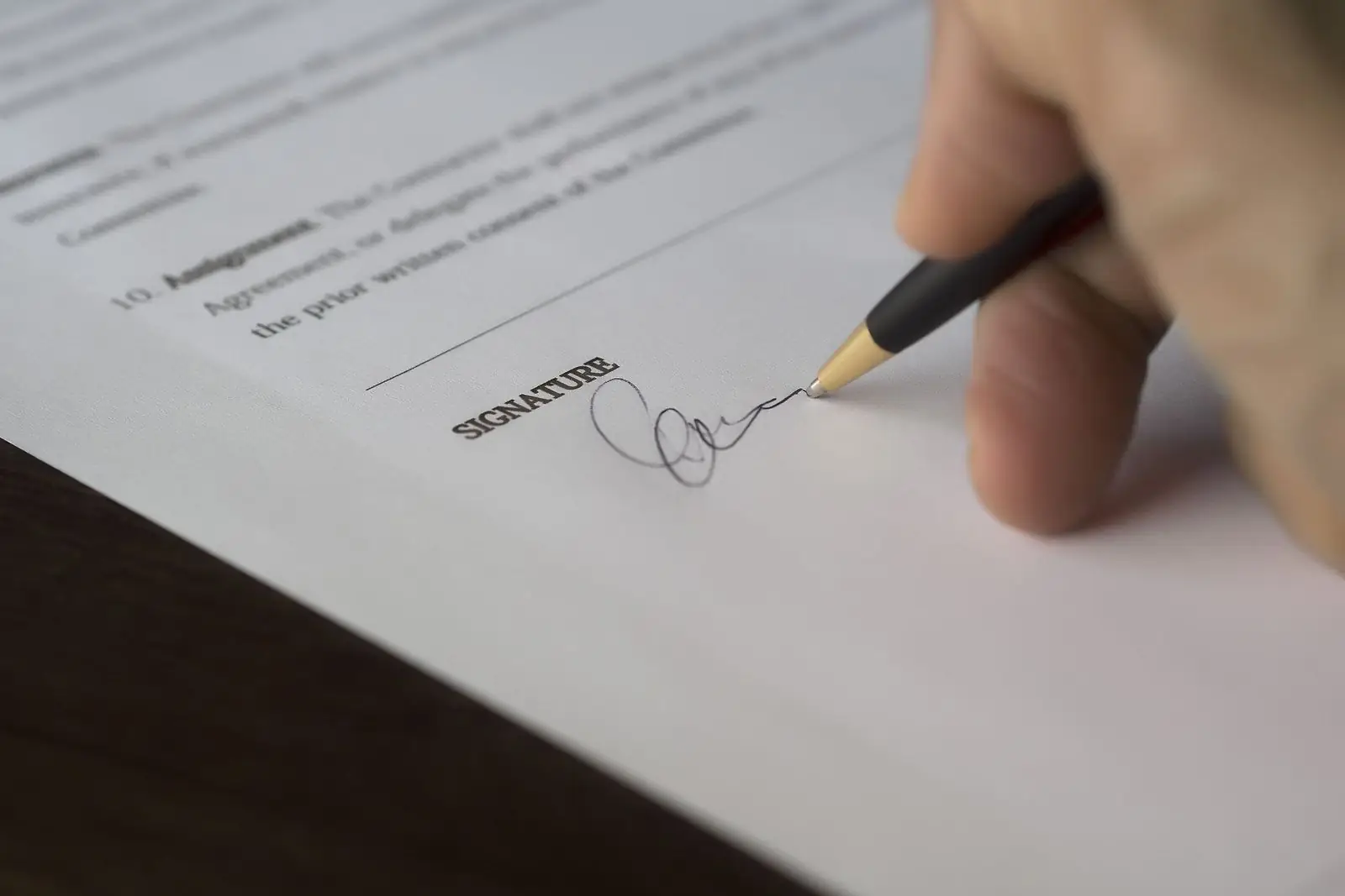Close-up of a hand signing on the signature line of a printed agreement