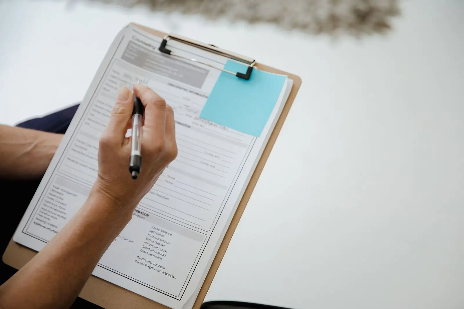 Hand filling in a printed form on a clipboard with a pen
